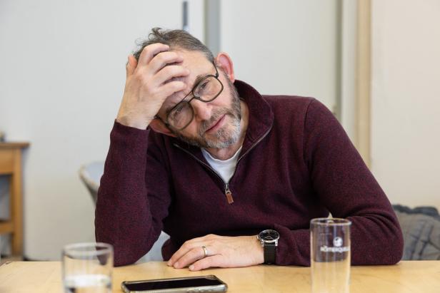 Ein Mann mit Brille sitzt an einem Tisch und wirkt nachdenklich.