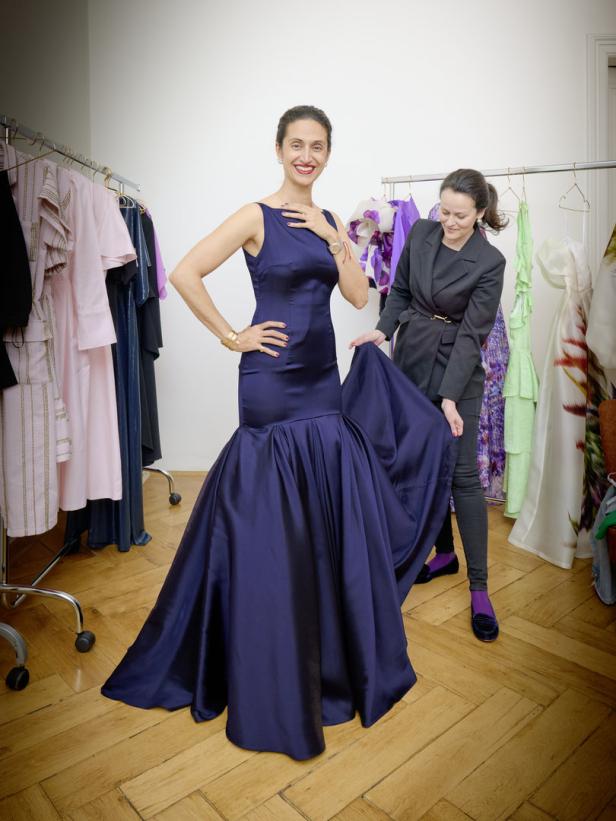 Eine Frau probiert ein elegantes, dunkelblaues Abendkleid an, während eine Schneiderin ihr hilft.
