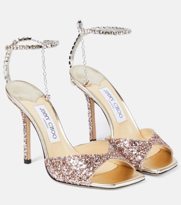 Zwei goldfarbene, glitzernde Jimmy Choo Sandalen mit Strass-Knöchelriemchen.