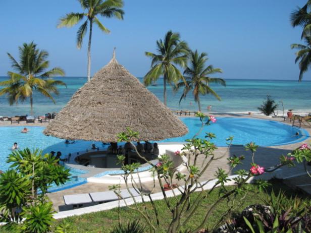 Ein Pool mit einer Bar unter einem Strohdach, umgeben von Palmen und dem Meer.