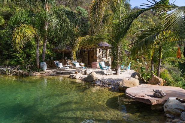 Ein Pool umgeben von Palmen und einem kleinen Steinhaus mit Liegestühlen.