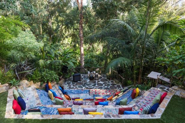Ein Amphitheater im Freien mit einer Bühne und Sitzplätzen mit bunten Kissen inmitten üppiger Vegetation.