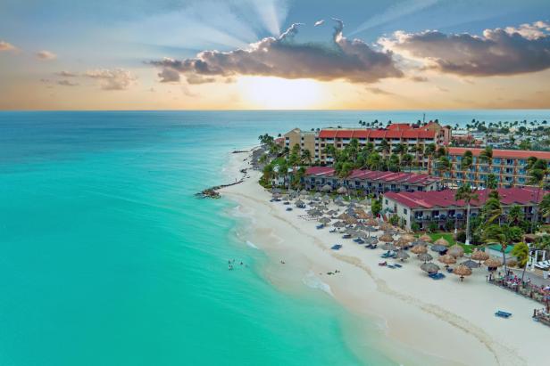 Luftaufnahme eines Resorts am Strand mit türkisfarbenem Wasser bei Sonnenuntergang.
