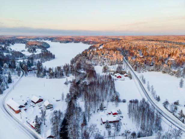 Luftaufnahme einer verschneiten Landschaft mit roten Häusern und einem zugefrorenen See.
