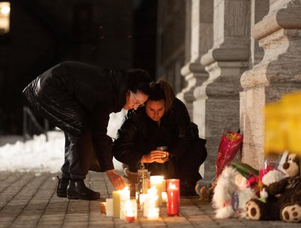 Zwei Frauen zünden Kerzen vor einem Gebäude an, umgeben von Blumen und Stofftieren.