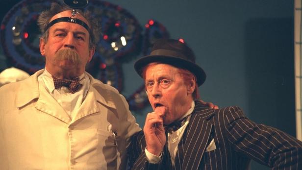 Zwei Männer in Kostümen stehen auf einer Bühne.