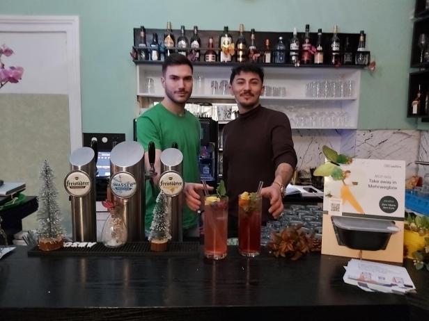 Zwei Barkeeper stehen hinter der Theke mit Getränken und Zapfhähnen.