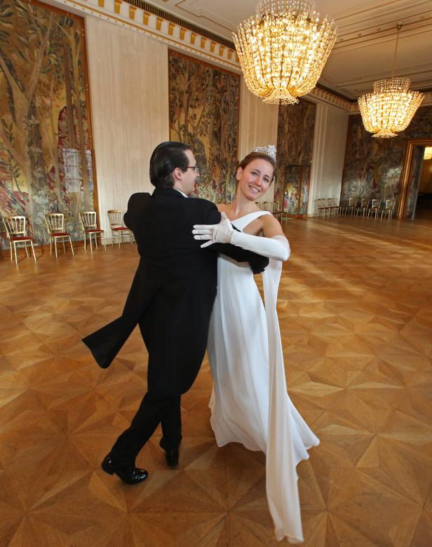 Ein Paar tanzt in einem Ballsaal mit Parkettboden und großen Wandteppichen.