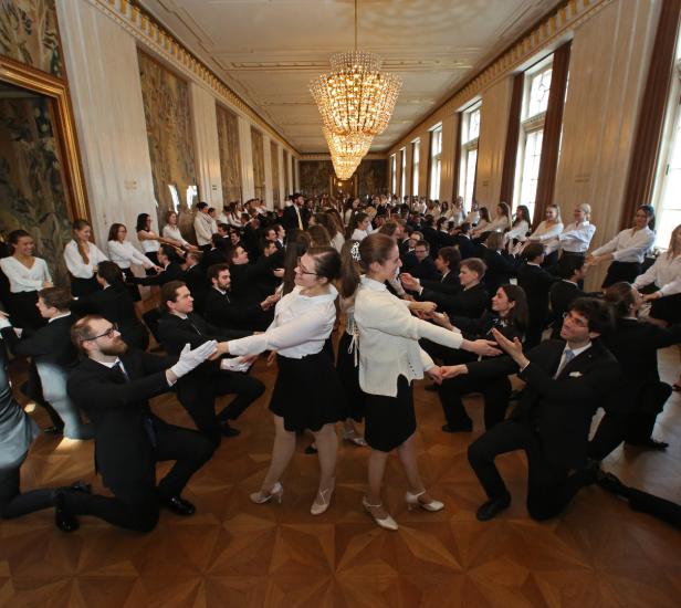Viele junge Leute tanzen in einem Ballsaal miteinander.