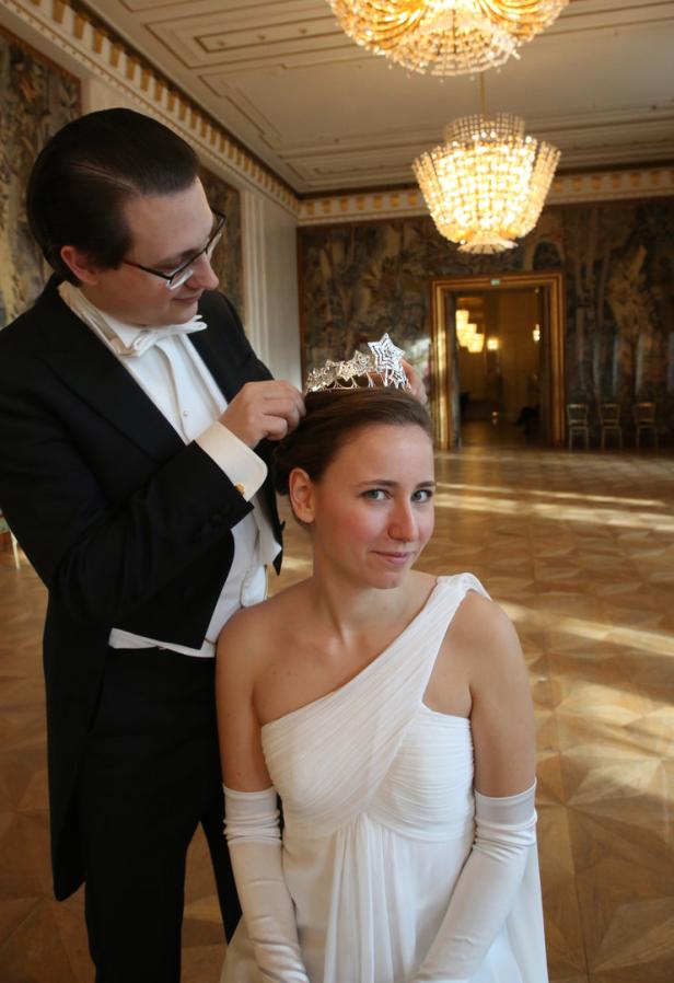 Ein Mann im Smoking setzt einer Frau im weißen Kleid eine Tiara auf.
