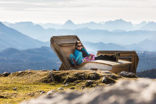 Eine Frau und ein Kind entspannen auf einer Liege mit Blick auf eine Berglandschaft.