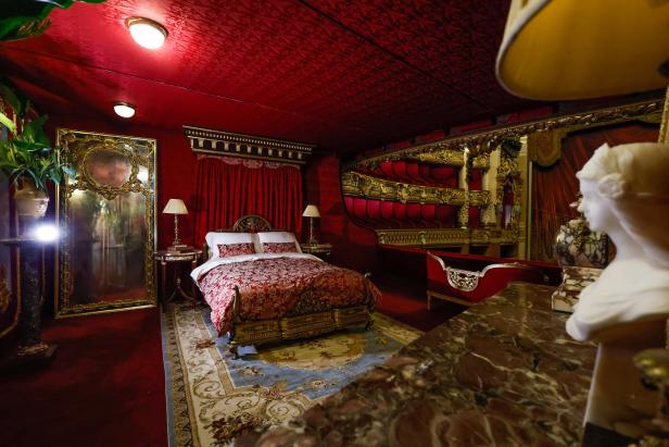 Ein opulent eingerichtetes Schlafzimmer mit rotem Teppich und einer Zuschauertribüne im Hintergrund.
