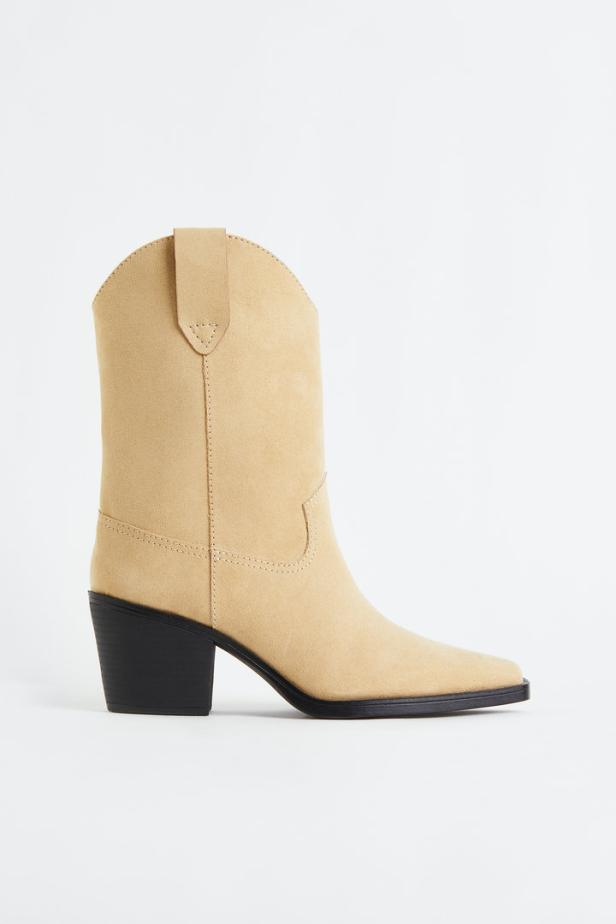 Ein beiger Cowboystiefel mit schwarzem Absatz vor einem weißen Hintergrund.