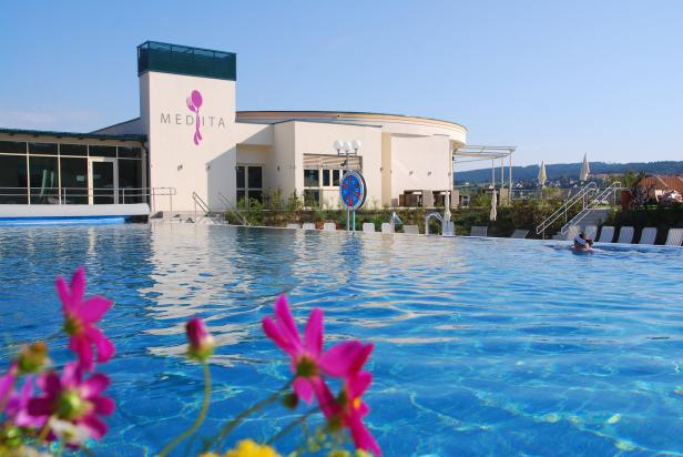 Das Medita Resort mit einem großen Außenpool und blühenden Blumen im Vordergrund.