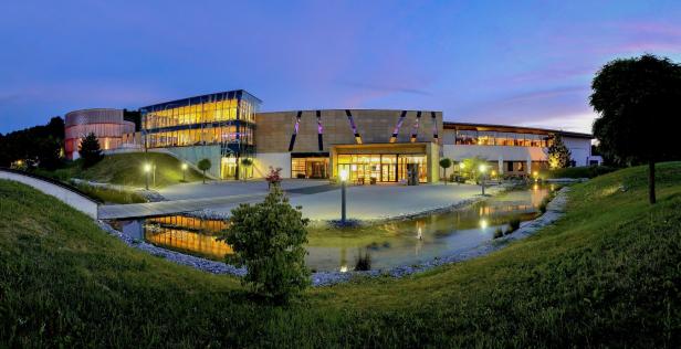 Das beleuchtete Gebäude des Lentos Kunstmuseums in Linz mit einem Teich im Vordergrund.