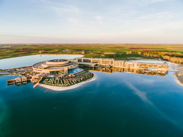 Luftaufnahme eines Resorts mit rundem Gebäude und Hotelanlage an einem See.