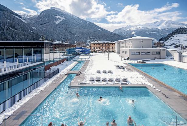 Menschen schwimmen in Außenpools im Schnee vor dem „Hotel Krone“ in den Bergen.