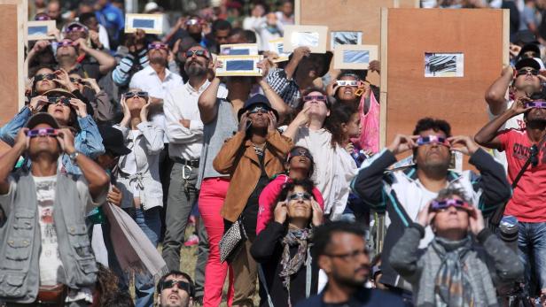 Eine Menschenmenge blickt mit speziellen Brillen oder Filtern in den Himmel, um eine Sonnenfinsternis zu beobachten.