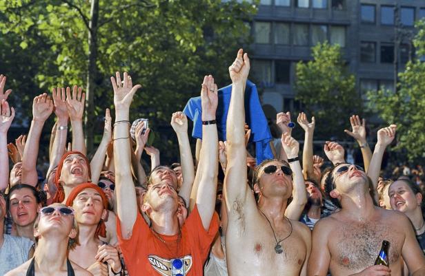 Eine Menschenmenge jubelt mit erhobenen Armen bei einem Open-Air-Konzert.
