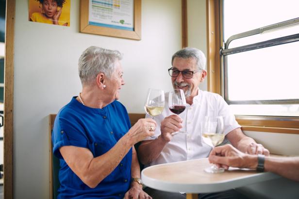 Seniorenpaar genießt ein Glas Wein in einem Zugabteil.
