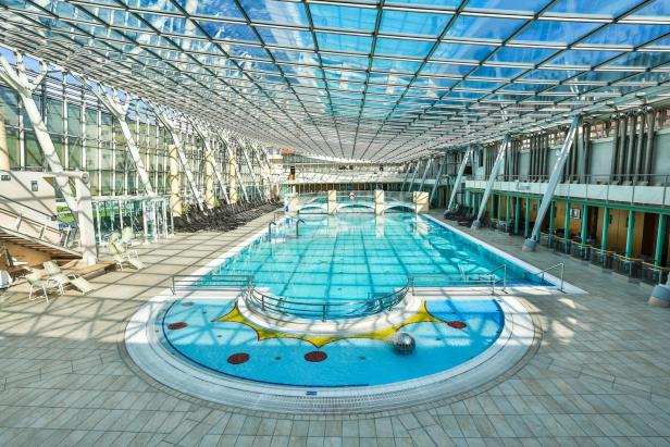 Ein großes Schwimmbad mit Glasdach und Liegestühlen an den Seiten.