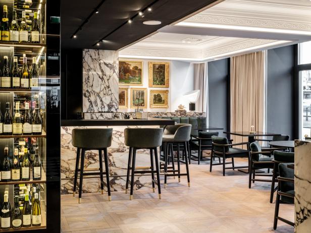 Eine Bar mit Marmortheke, Hockern und einem Regal voller Weinflaschen.