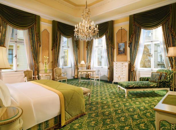 Ein luxuriöses Hotelzimmer mit einem großen Bett, einem Kronleuchter und grünen Teppichen.