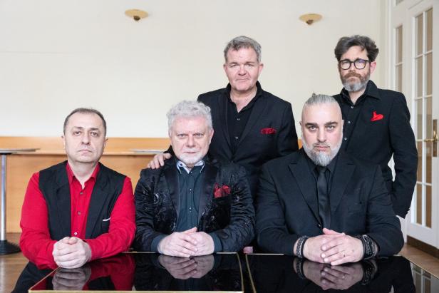 Fünf Männer posieren in Anzügen für ein Gruppenfoto.