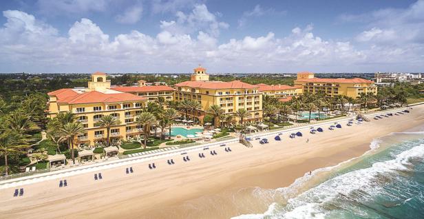 Ein großes Hotelresort liegt an einem Sandstrand mit Palmen und blauem Meer.