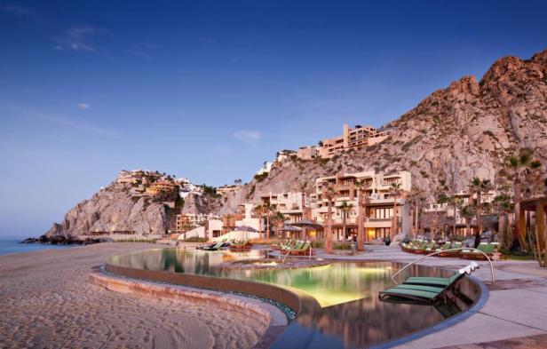 Ein Luxusresort liegt an einem Strand unterhalb eines felsigen Hügels.