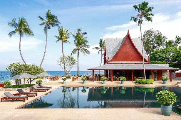 Ein Pool spiegelt ein Gebäude im thailändischen Stil und Palmen wider.