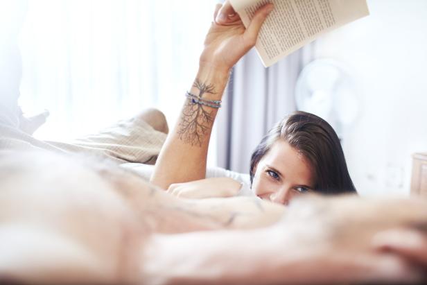 Eine Frau liegt im Bett und hält ein Buch in der Hand.