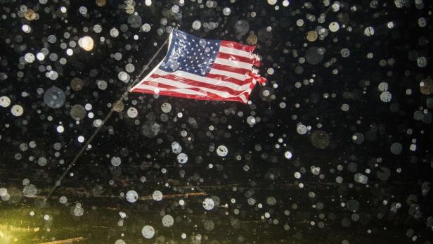 Eine beschädigte amerikanische Flagge weht im Wind, während Regentropfen fallen.