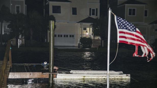 Eine amerikanische Flagge weht vor einem überfluteten Wohngebiet bei Nacht.