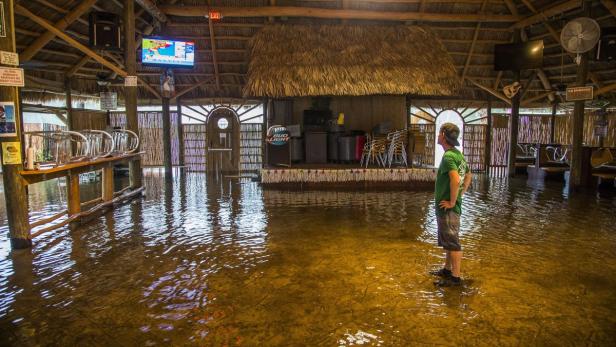 Ein Mann steht in einem überfluteten Restaurant mit Strohdach.