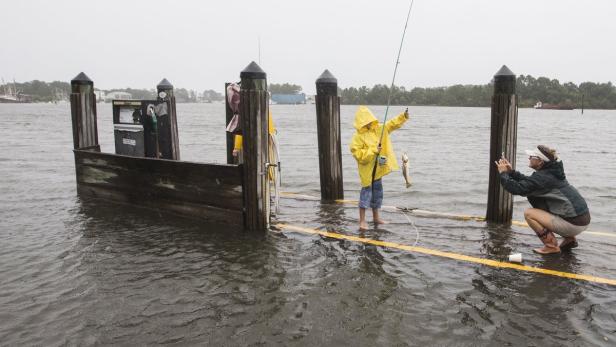 Ein Kind angelt im überfluteten Bereich, während eine Frau ein Foto macht.