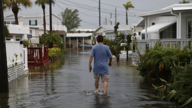 Ein Mann watet durch eine überflutete Straße in einer Wohngegend.