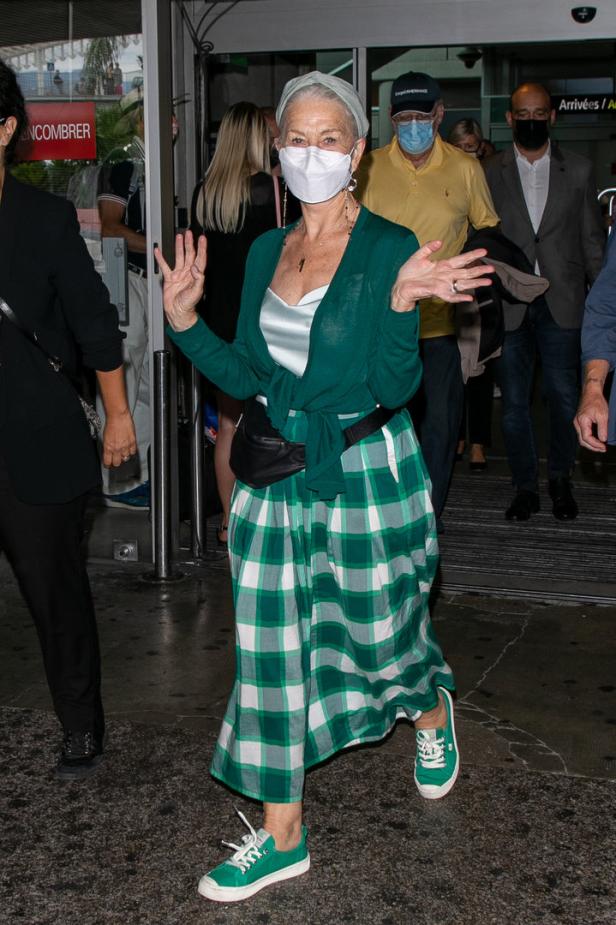 Helen Mirren verlässt mit Maske und grün kariertem Rock ein Gebäude.