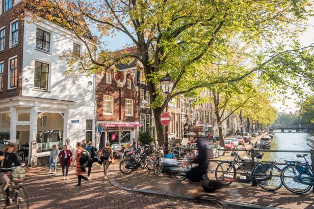 Herbstliche Straßenszene in Amsterdam mit Menschen, Fahrrädern und einem Kanal.
