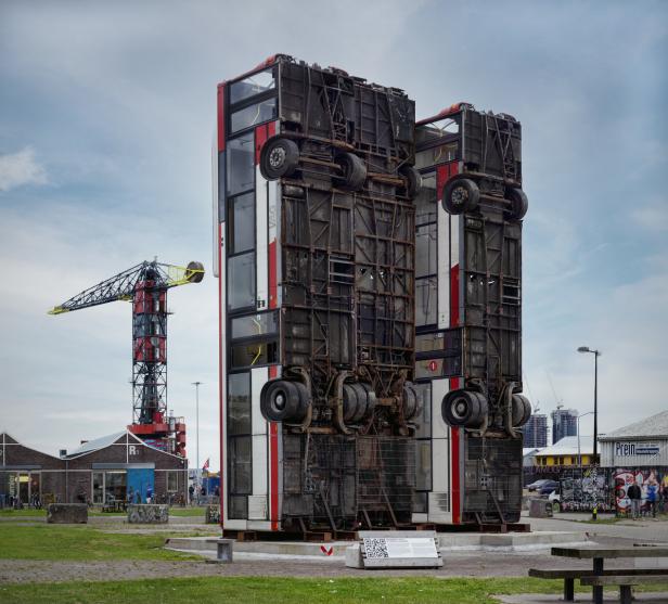 Eine Skulptur aus zwei aufrecht stehenden, umgedrehten Bussen in einem städtischen Park.