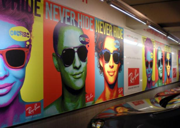 Mehrere Ray-Ban „Never Hide“-Werbeplakate in einem öffentlichen Raum.