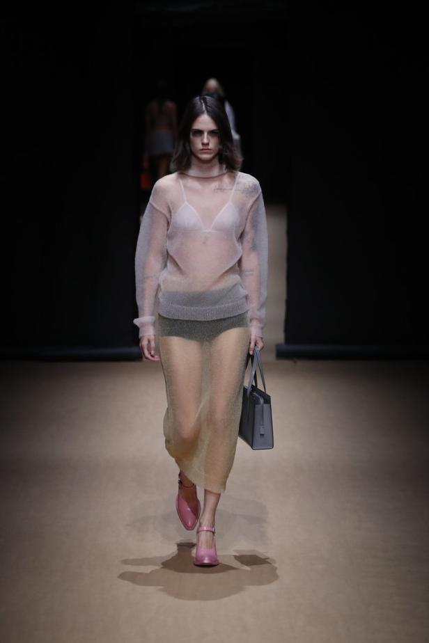 Eine Frau in einem transparenten Outfit mit Handtasche auf einem Laufsteg.