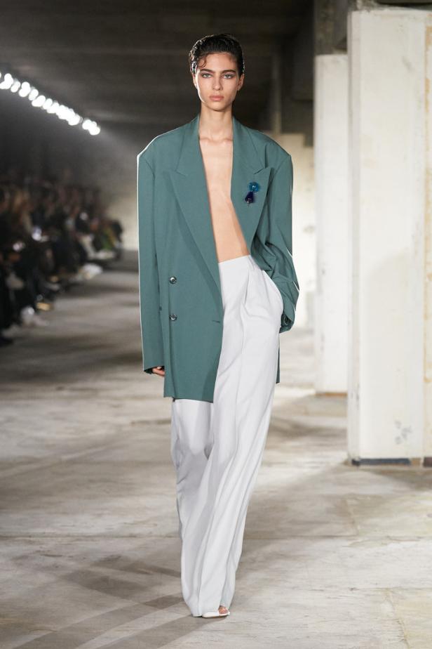 Eine Frau auf dem Laufsteg trägt einen grünen Blazer und eine weite, weiße Hose.