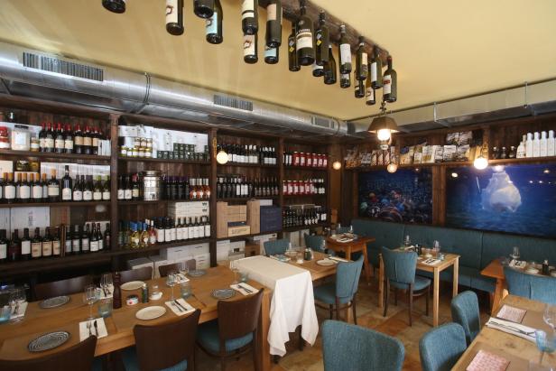 Innenansicht eines Restaurants mit Holzwänden, Regalen voller Weinflaschen und gedeckten Tischen.