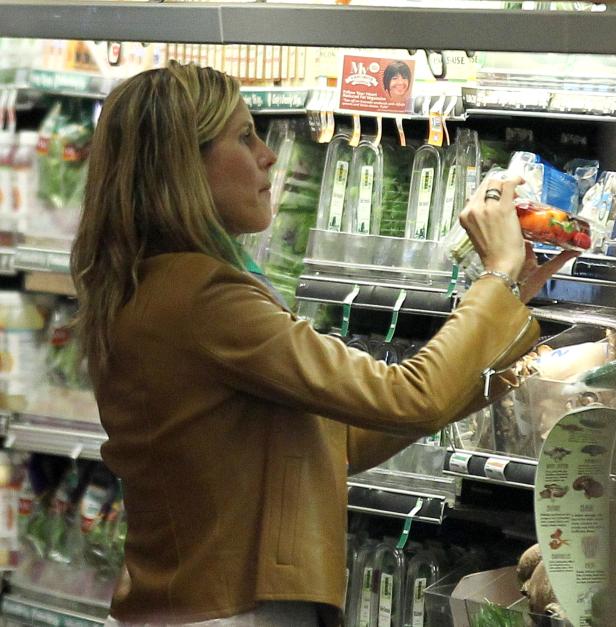 Eine Frau in einem Supermarkt wählt Paprika aus dem Gemüseregal.