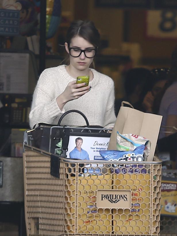 Emma Roberts steht mit einem Einkaufswagen in einem Pavilions-Supermarkt und blickt auf ihr Handy.
