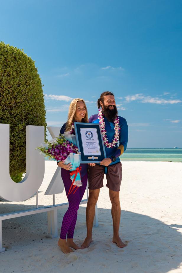 Ein Paar am Strand hält eine Urkunde von Guinness World Records und einen Blumenstrauß.