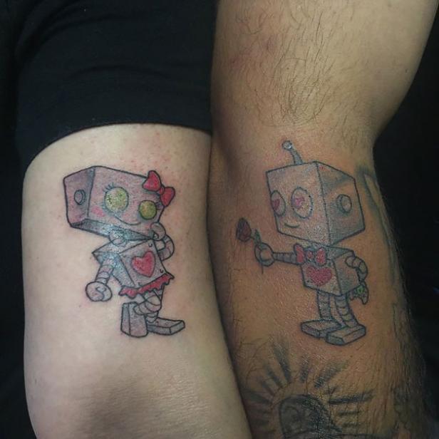 Zwei Arme mit passenden Tätowierungen von Roboterfiguren, ein Männchen mit Rose und ein Weibchen mit Schleife.