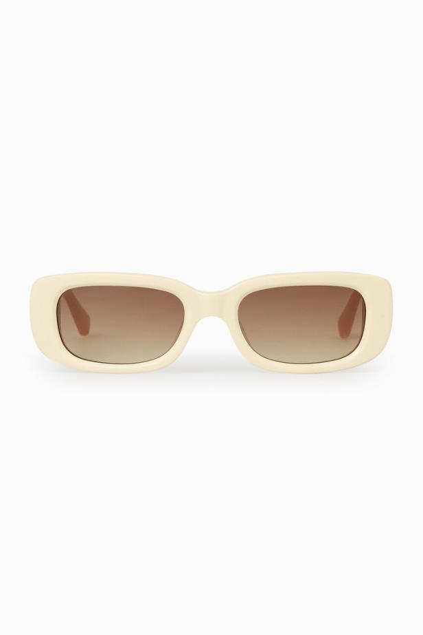Eine cremefarbene Sonnenbrille mit braunen Gläsern vor einem weißen Hintergrund.