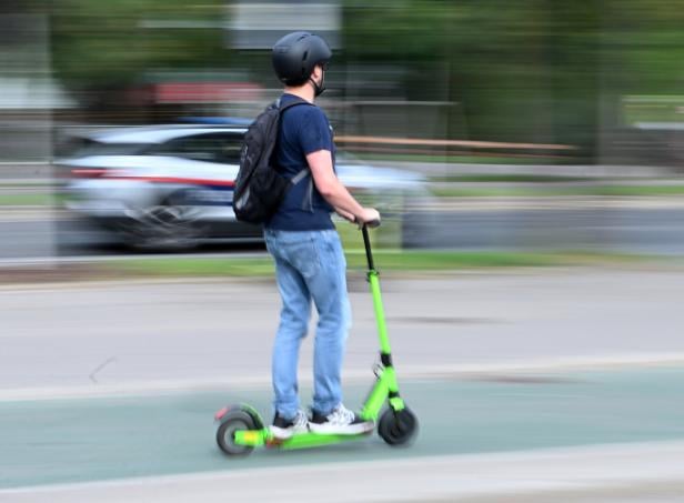 Ein Mann fährt mit einem grünen E-Scooter auf der Straße. Ein Mann fährt mit einem grünen E-Scooter auf der Straße.